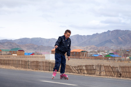 Mongolia Ulgii 2019-05-05 Mongolian boy in colorful clothes rides pink inline skates on road in...