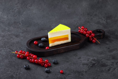 Piece of souffle lemon cake on wooden plate, with blueberry and red currant