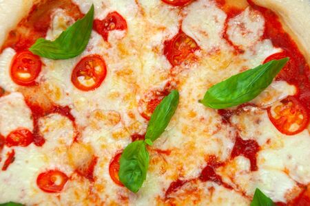 Fresh margarita pizza with cherry tomatoes, basil, mozzarella cheese on wooden vintage desk on black background, close-up, view from above, horizontalの写真素材