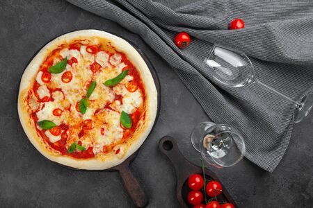 Glass of white wine and pizza margarita with tomatoes cherry, cheese and basil on wooden vintage desk, gray textile on black background, view from above, place for text, copy space, horizontalの写真素材