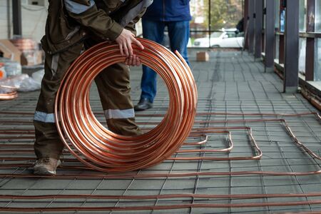 Plumber laying copper pipes on floor with warm heatingの写真素材