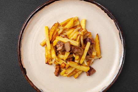 Fried potatoes with mushrooms and vegetables on dark background, top view