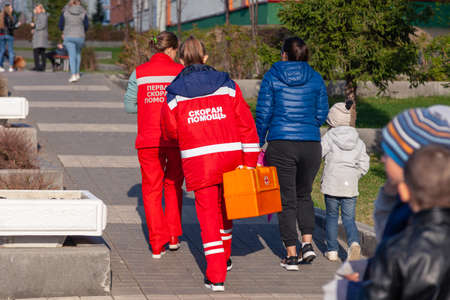 Russia Kemerovo 2019-05-21 Ambulance team of a woman in a red uniform with an orange medicine case is walking down the street in the park in the fall. Back viewの写真素材