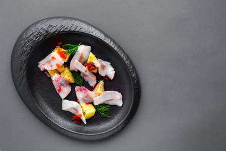 Cold appetizer salted herring with boiled potatoes on black plateの写真素材
