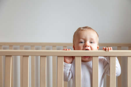 Blond cute little baby biting wooden bed headboardの写真素材