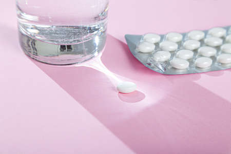 Water glass, blister with medical pills, tablets, vitamins on pink backgroundの写真素材