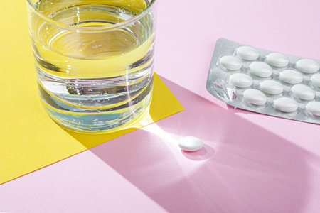 Water glass, blister with medical pills, tablets, vitamins on pink backgroundの写真素材