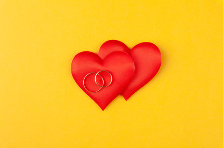 Two jewel round golden rings on red hearts, concept love, gift, proposal of marriageの写真素材