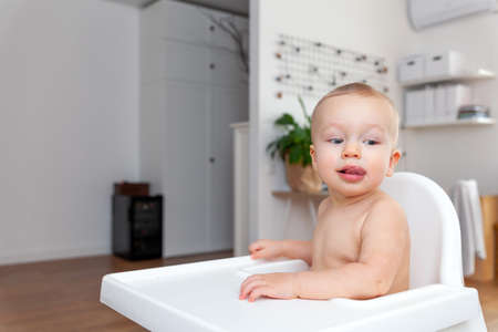 Funny blond baby infant sitting in chair and shows tongue, apartment backgroundの写真素材