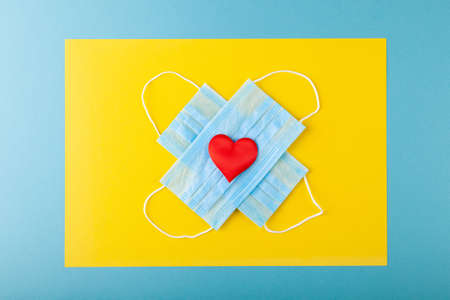 Red heart and anti-epidemic blue medical protective masks, concept valentines day, love, health care, thank to doctors, copy space, horizontal, top view, flatlyの写真素材