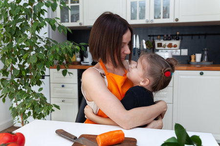 Little girl and beautiful mom are cooking vegetables at home kitchenの写真素材