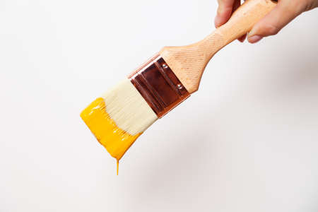 Hand with paintbrush with yellow paint drips off the brushの写真素材