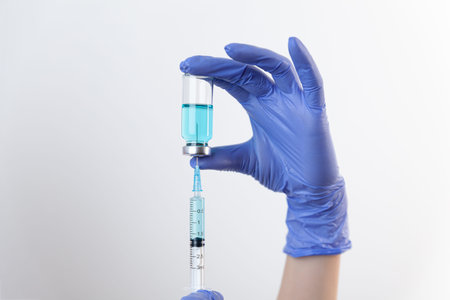 Doctor in gloves filling up syringe from bottle with vaccine, medicine