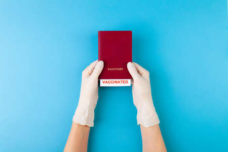 Hand in medical glove holding passport with vaccinated stamp on blue backgroundの写真素材