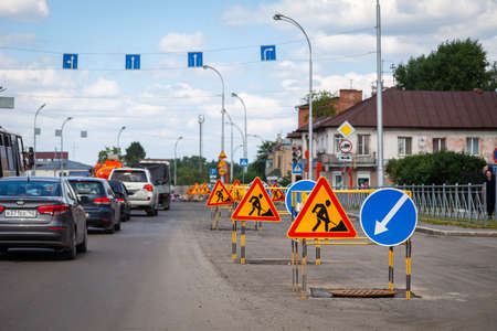 Russia, Kemerovo 2019-07-11 asphalt road repairs, yellow warning triangle signs about road works and bypass directionsの写真素材