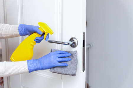 Hands in gloves disinfecting door handle with rag and spray detergentの写真素材