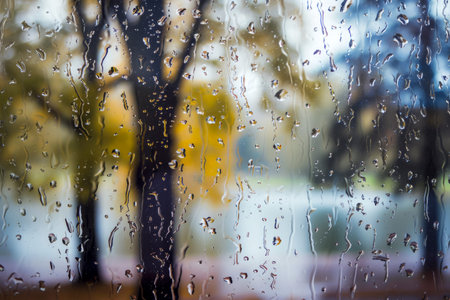 raindrops on the windows glass in focus with blurred autumn background. autumn leaves on rainy glass texture, bright natural backdrop. concept . AI generated.の素材