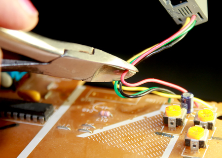 Electrical board with electronic components. High-tech printed circuit board. Cutting the electric wire with wire cuttersの写真素材