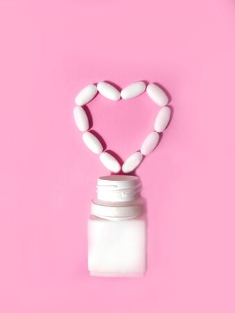 The pills are laid out in the shape of a heart near the bottle. On a pink background. Top view. Space for text.の写真素材