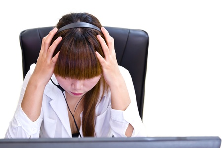 Young tired business woman with headache sitting at computer in workplace holding headの写真素材