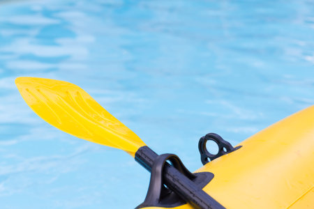 Close up yellow paddle, boat inflatable in refreshing blue swimming pool.