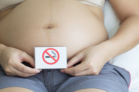 Pregnant woman holding label with smoking ban in bedroom background, unhealthy concept.の写真素材