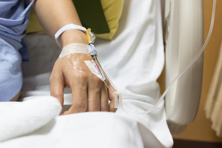 Asian woman patient is on drip receiving a saline solution on bed VIP room at hospital, selective focus and copy space white electronic bed background.の写真素材