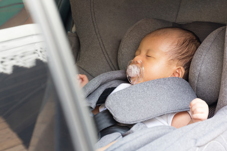 Asian cute newborn baby sleeping in modern car seat. Child new born traveling safety on the road. Safe way to travel fastened seat belts in a vehicle with young kids. Trip with an infant.の写真素材