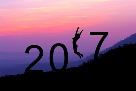 Silhouette young woman jumping over 2017 years on the hill at sunset, while celebrating new year.