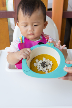 Asian cute baby eating food, Mother feeding solid food for young kid eight month at home.の写真素材