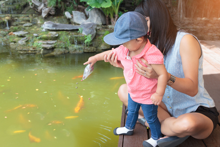 Asian beautiful mother is take care your cute baby feeding fish in garden,Activities to strengthen the love of the family.の写真素材