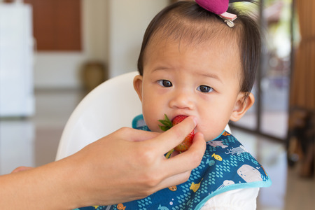 Asian cute baby eating fresh strawberry at home.の写真素材