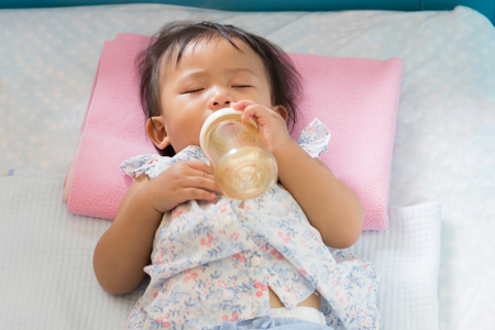 Asian cute baby is sleeping with milk bottle in mouth on the bed.の写真素材