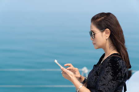 Rich business woman playing smart phone on luxury yacth in the ocean background, seniro women concept.の写真素材
