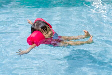 Asian cute little kid girl swimming in a pool, child enjoy floating on water in the summer time.の写真素材