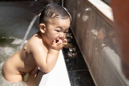 Asian happy laughing baby boy taking a bath playing with foam bubbles. Little child in a bathtub. Smiling kid in bathroom with sunlight window background. Hygiene and care for young children concept.の写真素材