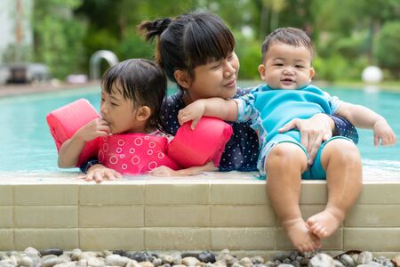 Asian cute little baby girl ans boy swimming from mother take care in pool, family daughter and son, children learning to swim lessons and early development concept in summer time.の写真素材