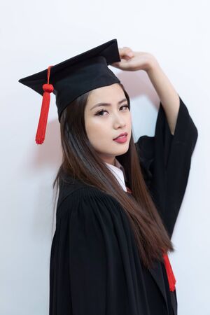 Portrait closeup. Asian beautiful smiley graduate graduated student girl young woman in cap gown on isolated white background wall. Celebrating graduation ceremony concept.の写真素材