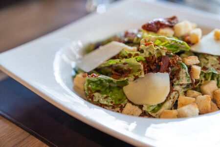 Fresh caesar salad in white plate on wooden table, in luxury restaurant. Close up.の写真素材