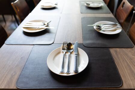 Silverware with forks, knives, plates on the wood table in restaurant served for dinner. Table setting on a big luxury table concept.の写真素材