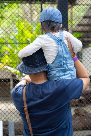 Cute baby girl and father looking animal in cage background, summer vacation holiday travel, family life style concept.の写真素材