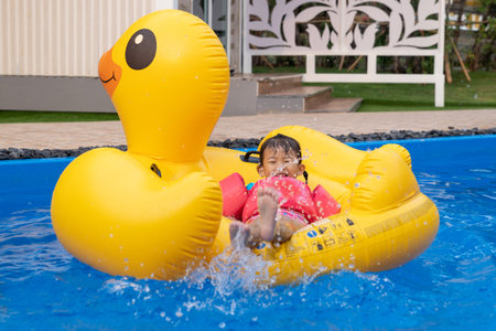 Asian cute little toddler girl in a colorful swimming suit relaxing on an inflatable toy ring...
