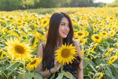 Cheerful multiracial Asian cute young woman joyful, smiling with sunflowers background. Happy carefree summer beautiful girl in sunflower field in spring.の写真素材
