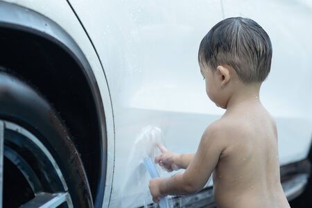 Asian child baby boy washing car, wash with luxury white car at home, in the garden on summer day.の写真素材