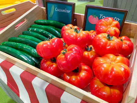 Artificial cucumbers and tomatos in a wooden box as a market design on the background of other vegetables and fruits, soft focus.の写真素材
