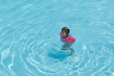 Asian cute little toddler girl in a colorful swimming suit relaxing in a pool having fun during summer vacation in a tropical resort.の写真素材