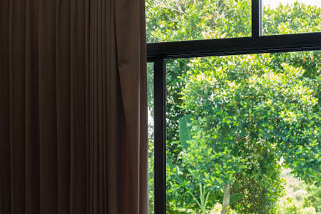 Modern brown curtain in room closed half way in sun shine through from balcony of outdoor garden backyard.の写真素材