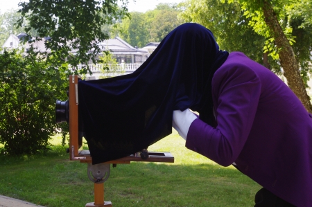 a man in purple tailcoat taking picture with an old wooden camera on a tripodの写真素材