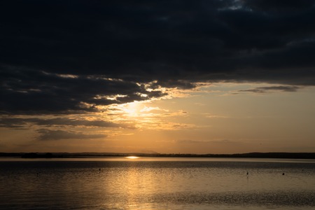 sunset over the water is hidden behind cloudsの写真素材