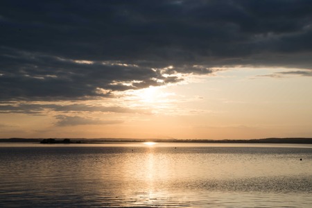 sunset over the water is hidden behind cloudsの写真素材